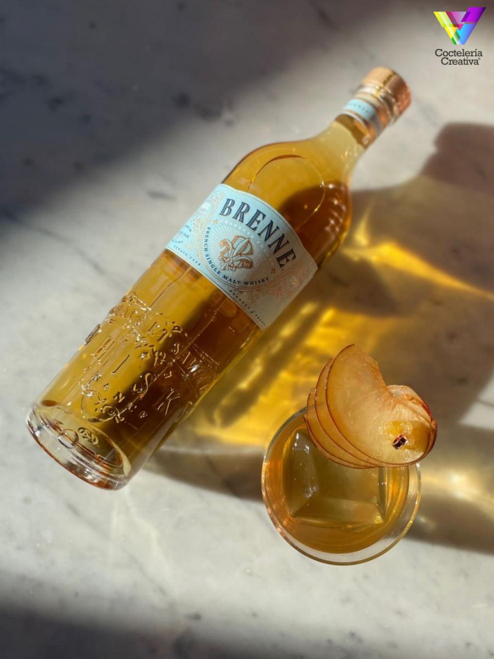 Botella de Brenne con copa con cocktail decorado con abanico de rodajas de ciruela