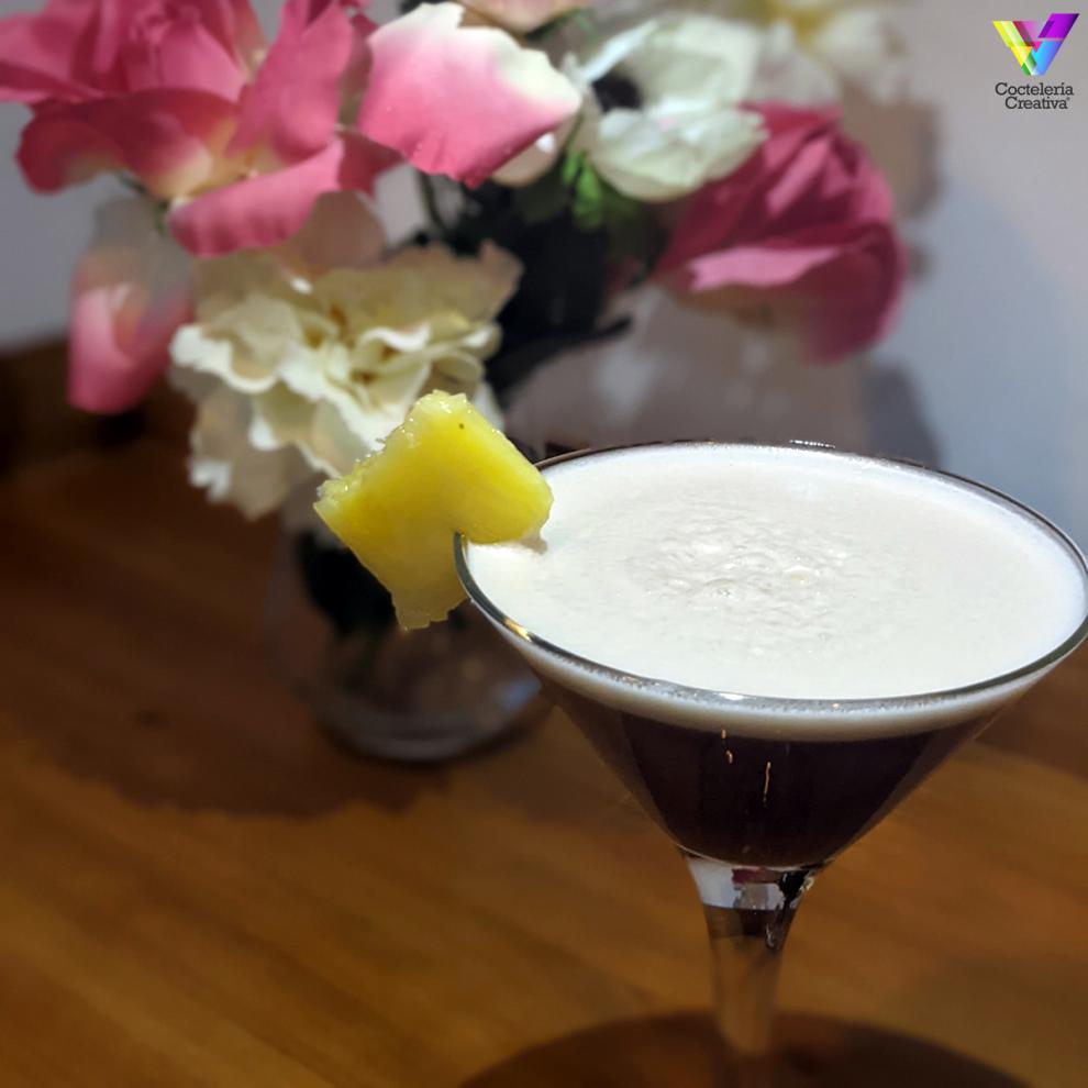 Copa de martini con Kintyre Tropical Martini decorado con trozo de piña y fondo de rosas