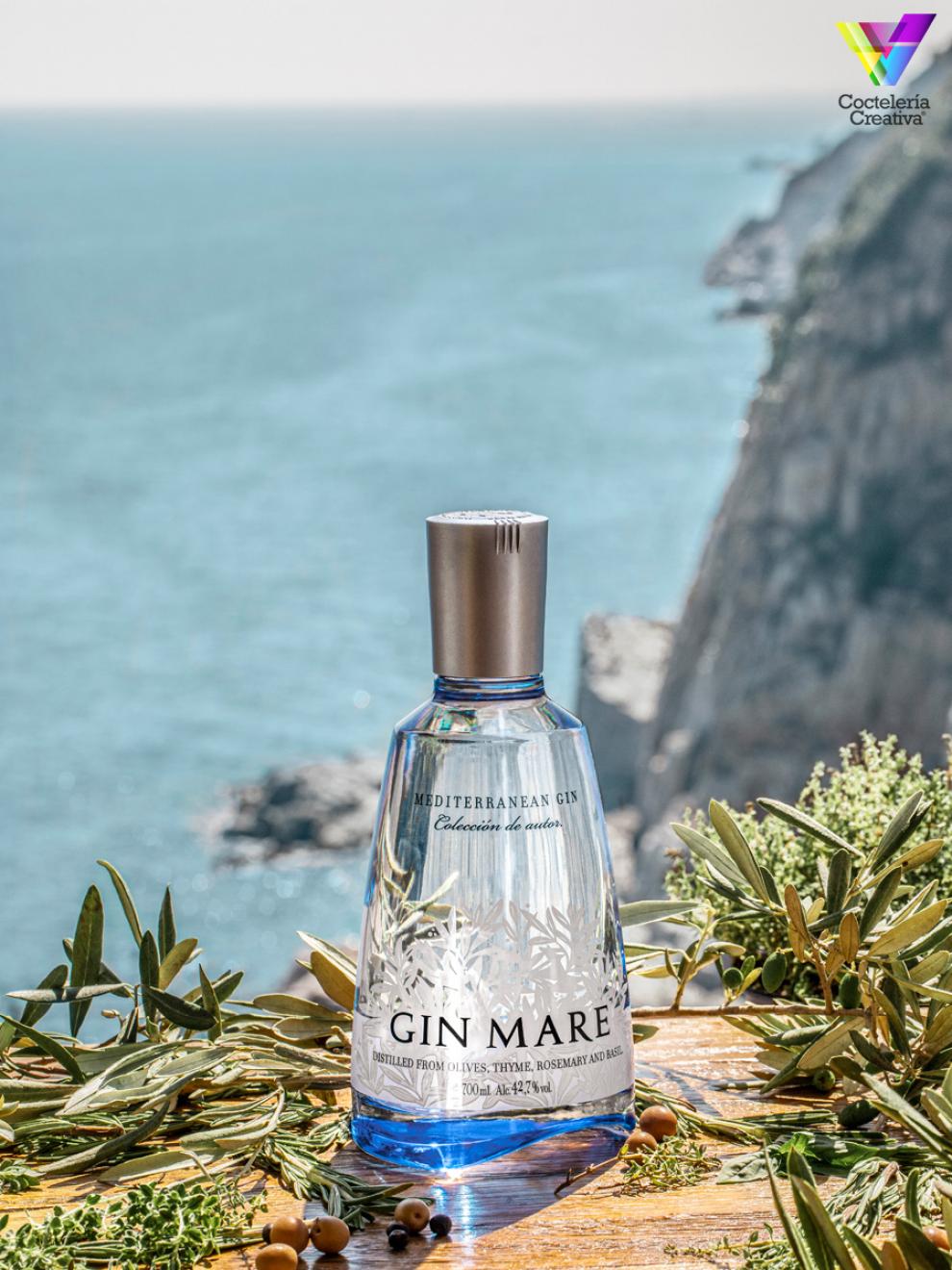 Botella de Gin Mare con botánicos con fondo de mar en el horizonte