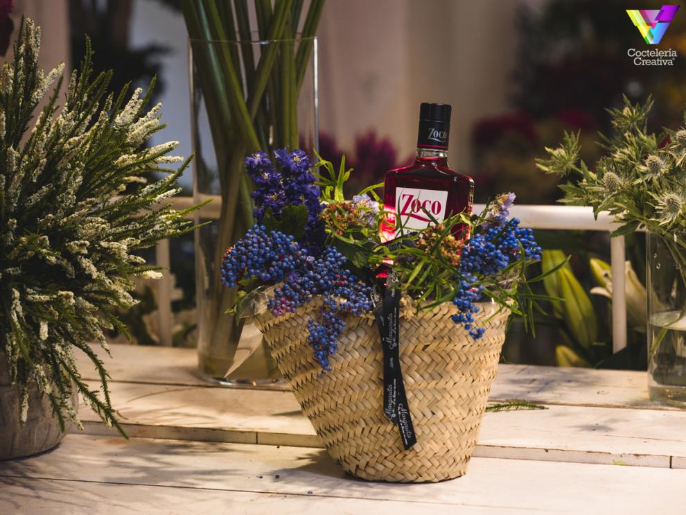 Canasta con arreglo floral y botella de Pacharán Zoco